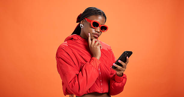 istock Woman, phone and texting in studio with thinking, chat and reading post on app on orange background space. Black person, mobile and notification with contact, scroll and choice on social network 2227855662