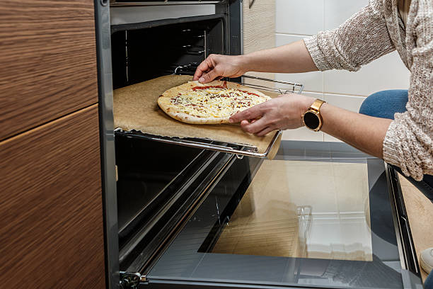 istock Woman places ham and cheese pizza into a modern oven for baking in a stylish kitchen setting 2227856410