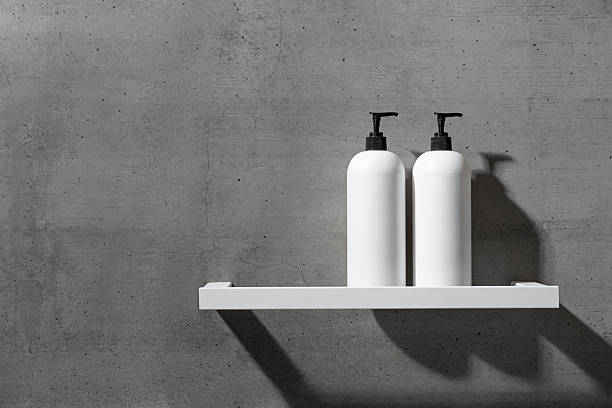 Two minimalist white bottles with black pump caps on white shelf against texture gray concrete background. Neutral tones minimalist interior design bathroom. Skincare, body care, beauty products
