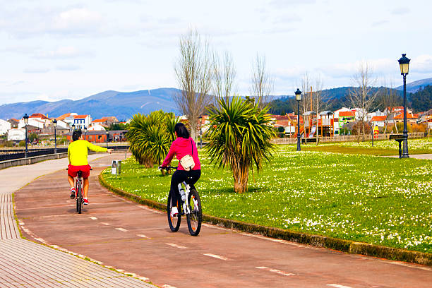 Young couple cycling along waterfront promenade garden. Noia,  A Coruña province, Galicia, Spain.