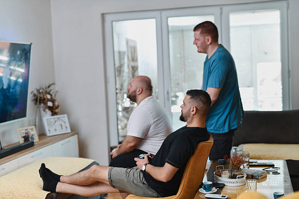 istock Group Of Friends Watching Screen As Two Are Competing And One Is Observing With Focus 2227864199