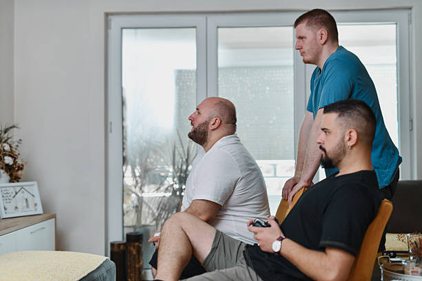 Intense Gaming Match Between Two Guys As Enthusiastic Friend Is Watching From Behind