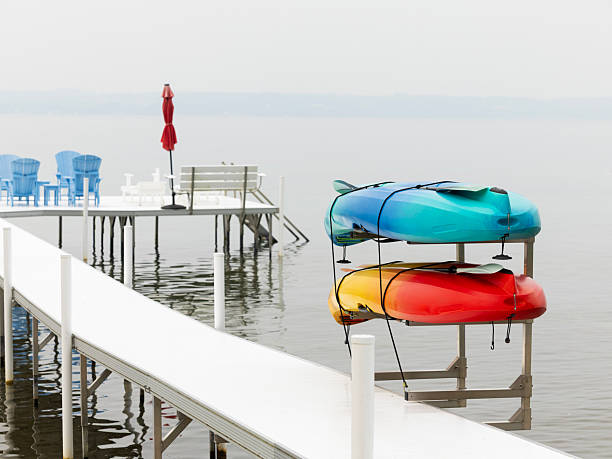 With their bright red, yellow and blue colors standing out against the background,  two kayaks are stored on a scaffold attached to a dock on Little Traverse Bay, Michigan, USA. With their paddles nearby , the boats can  be used for summer extreme water sport as well as rest, leisure, adventure and entertainment on the Lake Michigan bay.