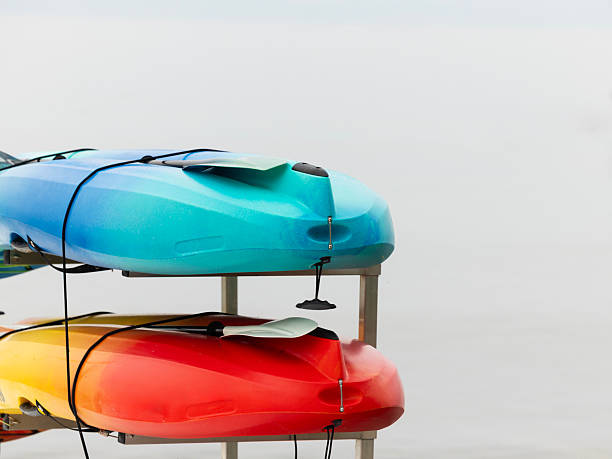 With their bright red, yellow and blue colors standing out against the background,  two kayaks are stored on a scaffold attached to a dock on Little Traverse Bay, Michigan, USA. With their paddles nearby , the boats can  be used for summer extreme water sport as well as rest, leisure, adventure and entertainment on the Lake Michigan bay.