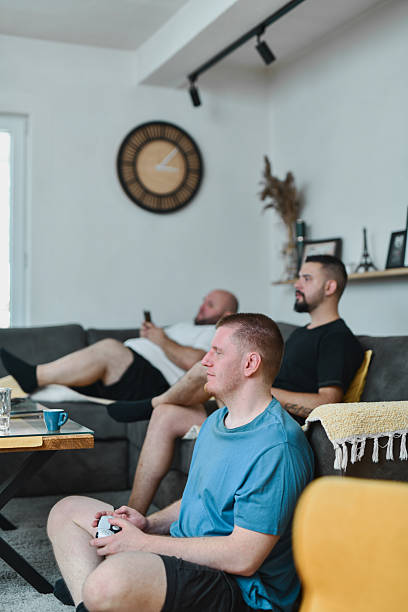 istock Relaxed Male Friends Sitting Around Console Playing Engaging Video Game In Cozy Shared Space 2227867508