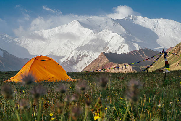 Bright yellow tent stands alone on green grass at 3600m Base Camp with vast panoramic view of Pamir mountains with Lenin Peak. Active people concept. Lenin peak expedition  in Kyrgyzstan, Central Asia