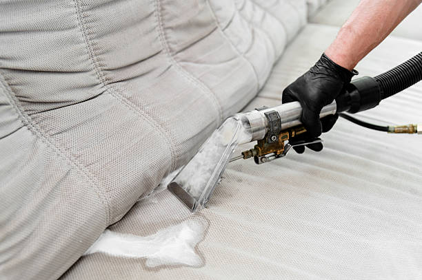 Professional upholstery cleaning service in action at residential home during daylight hours A technician is using specialized equipment to clean a fabric sofa in a living room. The process includes applying cleaning solution and extracting dirt. deep cleaning services stock pictures, royalty-free photos & images