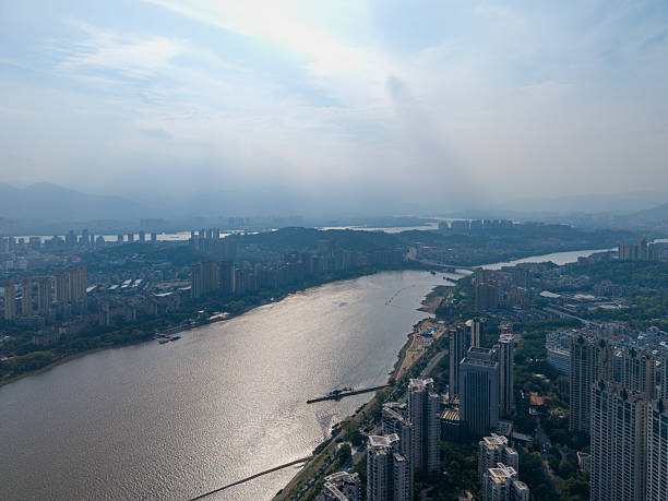 A bird's-eye view captures an urban waterfront park with lush greenery, adjacent to a bustling cityscape. The visual style is vibrant and dynamic, showcasing the contrast between nature and architecture. This image could be used for real estate promotions, travel guides, or urban planning presentations.