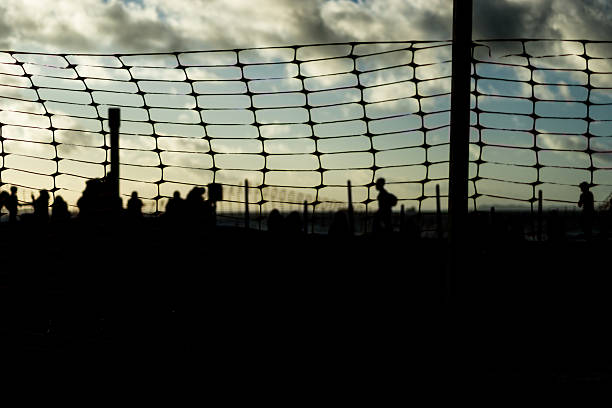 istock Unidentified people blurred in silhouette behind a plastic fence during a dramatic sunset. Winter season. 2227872862