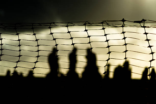 Unidentified people blurred in silhouette behind a plastic fence during a dramatic sunset. Winter season. Tourists traveling.