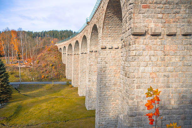 On a sunny autumn day, the impressive railway viaduct in Smrzovka stands tall against a backdrop of colorful foliage in the Jizera Mountains, inviting travelers to explore the stunning landscape.