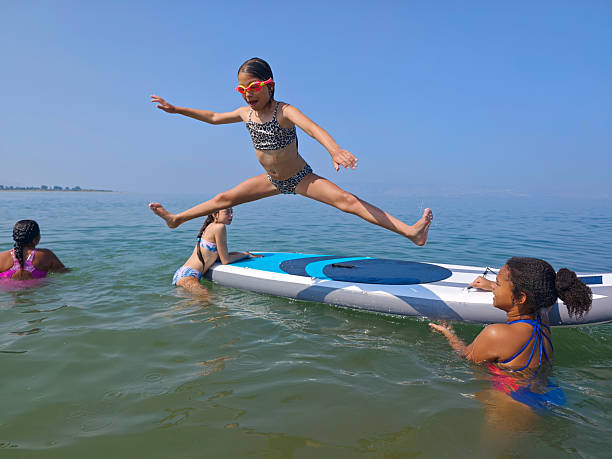 Energetic Girl Jumping in Split Pose Off Paddleboard into the Sea.