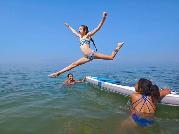 istock Young Girl Performing Mid-Air Split Jump from Paddleboard on a Sunny Day. 2227877448