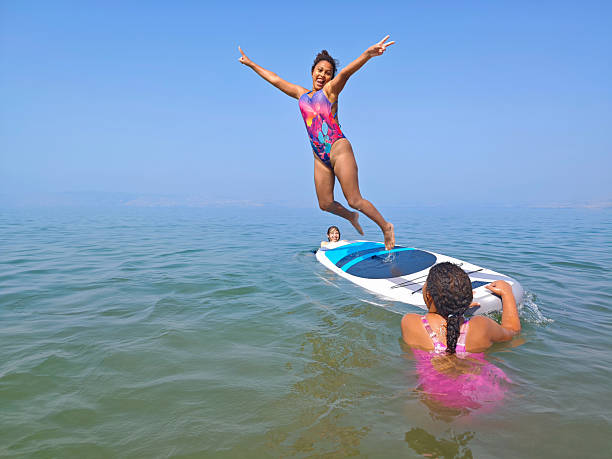 istock Joyful Girl Leaping from Paddleboard with Peace Sign on Summer Day. 2227877456