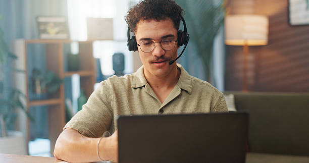 istock Man, consultant or remote worker with headset on laptop for online advice or communication at home. Male person, agent or virtual assistant with computer for desktop support, help or service at house 2227880415