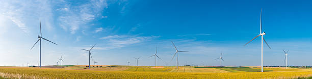 Wind turbines generating renewable electricity above farmland below big blue summer skies.