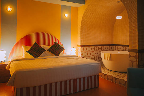Stylish hotel room interior featuring a retro-inspired design with patterned tiles, a round freestanding bathtub, curved ceiling, and warm ambient lighting. A cozy bed and unique lamp add to the inviting atmosphere. Captured in a boutique hotel with a nostalgic yet modern aesthetic.