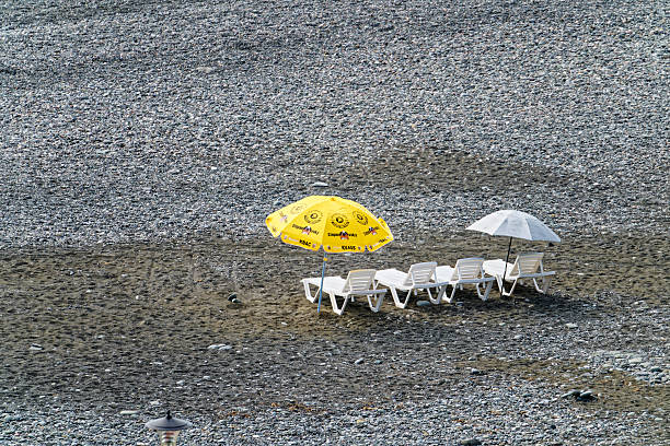 Batumi, Adjara, Georgia 24 June 2025: A peaceful Black Sea beach in Batumi with rows of empty sun loungers and colorful umbrellas scattered across the pebbled shore. A few vacationers relax under the shade, enjoying a quiet day by the sea.