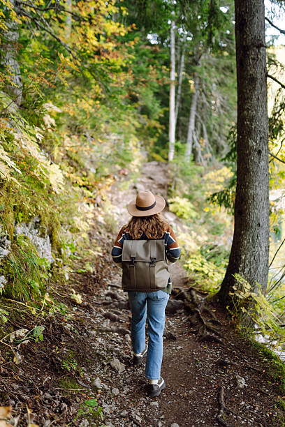 istock A young woman with a backpack and a hat walks along a rocky path in a dense forest. 2227892179
