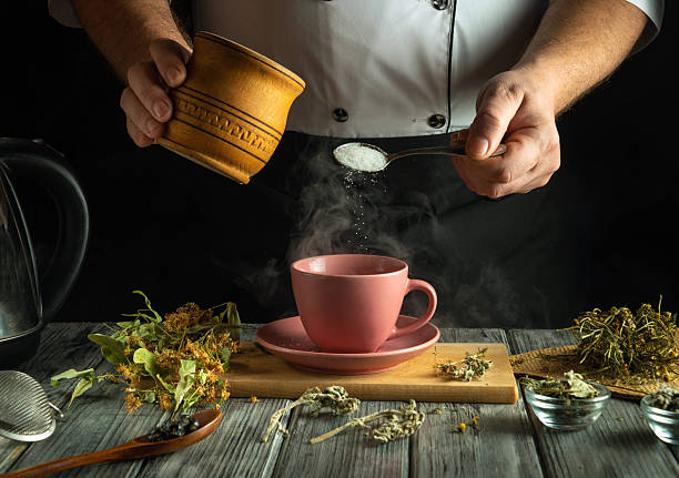 istock Hands skillfully add sugar to a steaming cup of herbal tea, surrounded by fresh herbs and kitchen tools. The warm ambiance highlights a tranquil evening ritual 2227892255