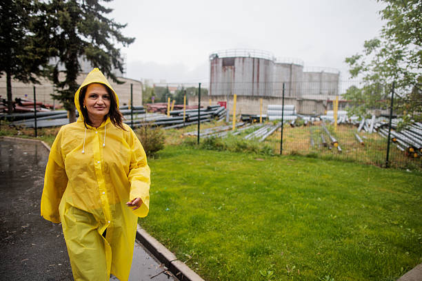 Middle-aged woman wearing a yellow raincoat walking purposefully through the rain-soaked streets.