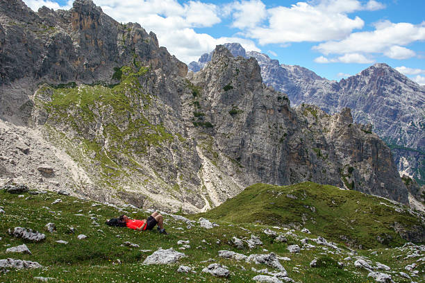 A hiker rests on a high-altitude meadow among the peaks of the Dolomites.