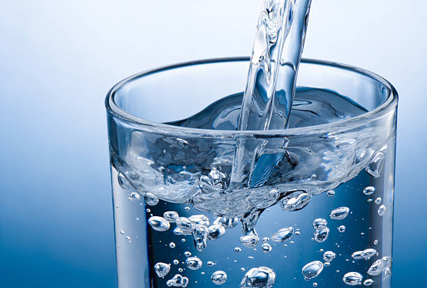 istock Pouring water into glass on blue background 2227897481