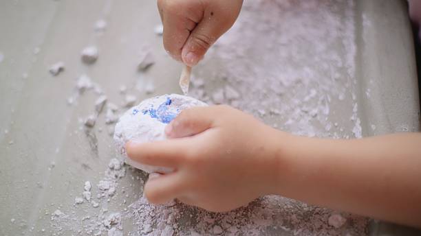 enthusiastic young Asian boy engages in a fun and educational activity, carefully excavating a toy dinosaur egg to discover the hidden dinosaur inside — combining play with learning and imagination.