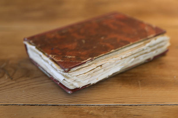 A Close-Up of an Old Handmade Book With Torn and Worn Pages Resting on a Rustic Wooden Table. The Scene Evokes History, Knowledge, and the Passage of Time.