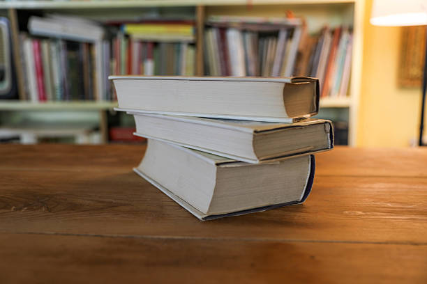 A Small Stack of Worn Hardcover Books Neatly Placed on a Wooden Table, With a Cozy Home Library Full of Bookshelves in the Background. The Scene Suggests Quiet Study, Reading, and a Love for Knowledge and Literature.