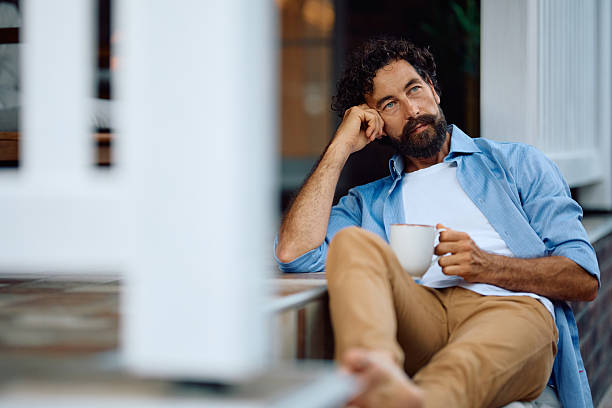 Pensive man having a cup of coffee while relaxing on a patio at home.
