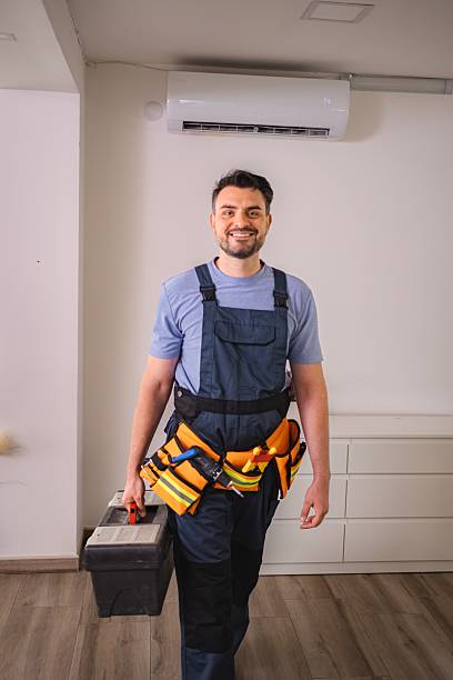Technician smiling carrying toolbox and wearing tool belt with air conditioner in background