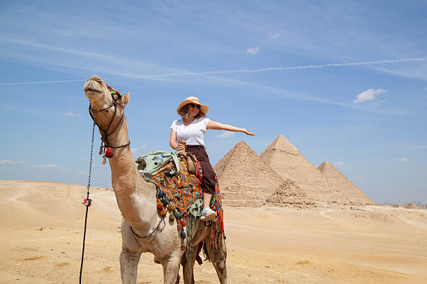 Young female tourist riding camel in the Egyptian desert and visits the Pyramids in Cairo stock photo