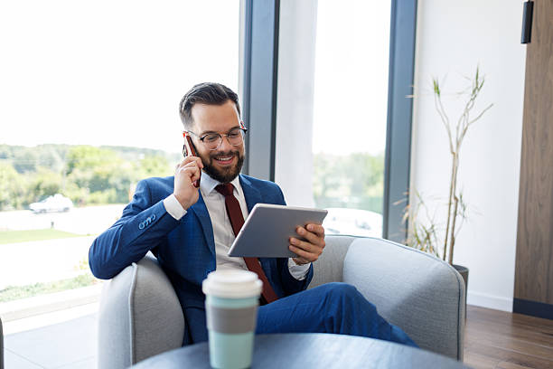 istock Businessman working on tablet and talking on phone in office lobby 2227915645
