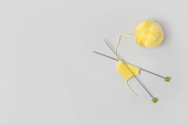 Yellow knitted wool on gray background with knitting needles for knitting warm clothes and hobbies needlework