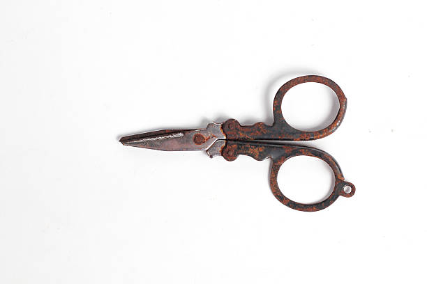 one large brown iron rusty scissors sticking out of a gray wooden board on a summer street
