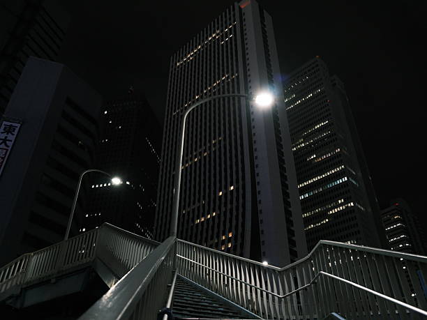 Steel stairs and a single streetlamp rise toward glass office towers, creating strong leading lines and deep negative space. Great for concepts of security, infrastructure, resilience, business district and modern architecture.