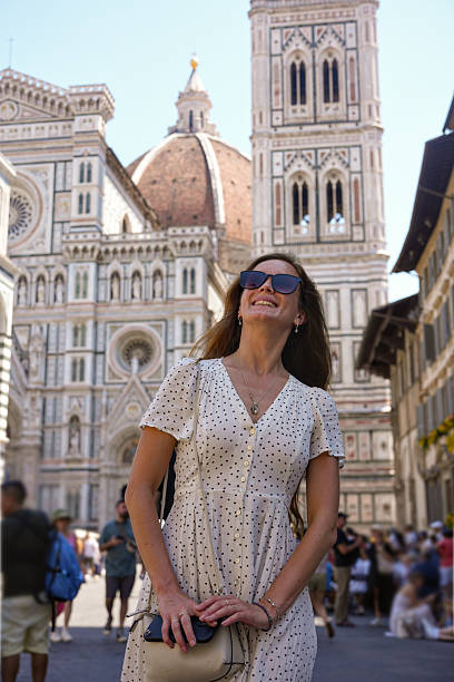 Smiling female tourist in polka dot dress posing near Florence Cathedral and Giotto's bell tower in Italy