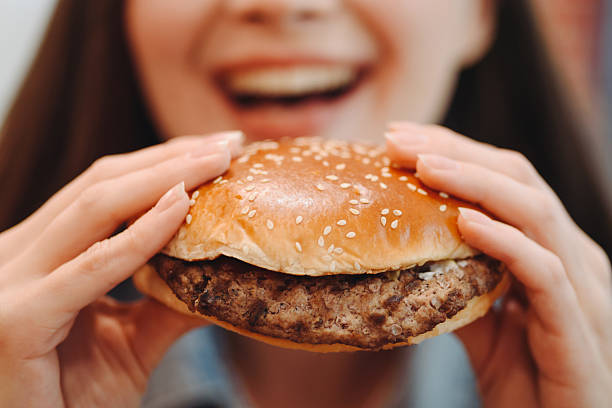 istock hamburger in hands, closeup view, young woman eats hamburger 2227933932