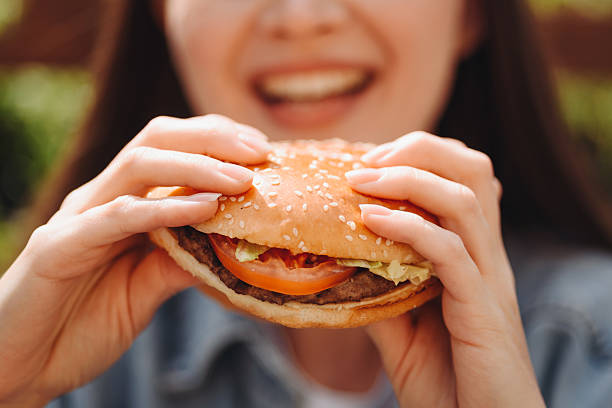 istock hamburger in hands, closeup view, young woman eats hamburger 2227933937