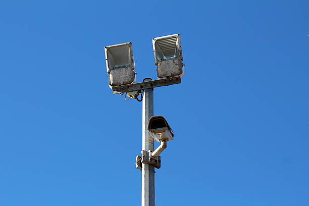 istock Outdoor floodlights and security camera on tall metal pole under clear sky 2227936332