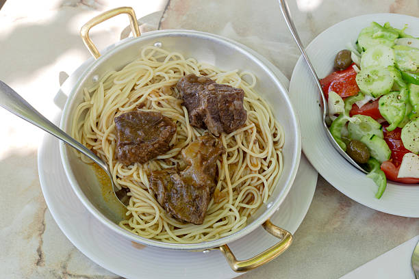 Stewed beef with pasta in bowl and salad (Greek cuisine) close-up on table in street tavern