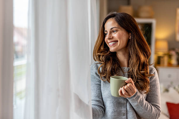 istock Smiling Woman Sipping Coffee While Looking Out a Window 2227949321