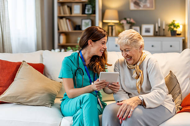 istock Smiling Nurse Assisting Elderly Woman During Home Visit Using Tablet 2227949356