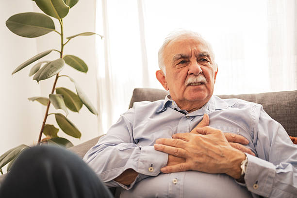 istock Senior man holding chest while seated on couch at home with natural lighting 2227952494