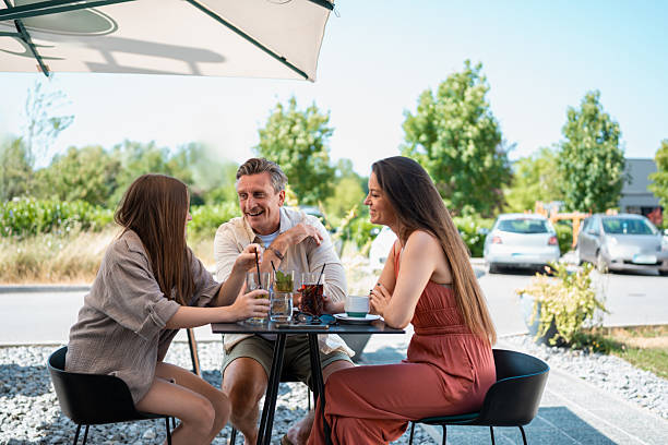 istock Young Friends Sharing Drinks And Laughter At Sunny Outdoor Cafe Table 2227953747