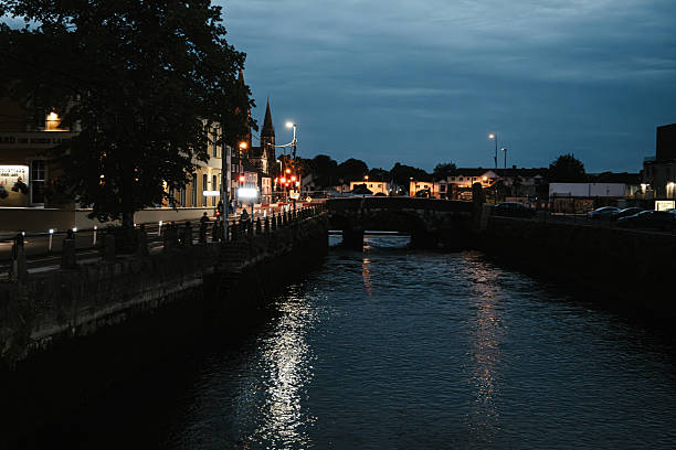 July 24, 2025 Cork, Ireland  A tranquil riverside scene capturing a charming town at dusk with soft reflections shimmering on the water