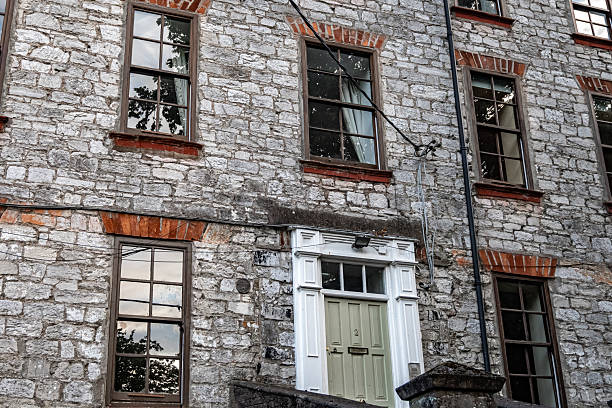 July 25, 2025 Cork, Ireland An old stone building, featuring vintage windows and a classic white door, conveys a profound sense of history