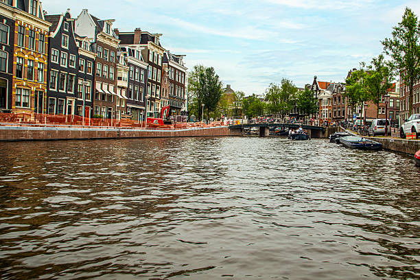 July 15, 2017 Amsterdam, Netherlands Typical canal in the city of Amsterdam with historic buildings on both sides, parked bicycles and a tourist boat sailing on the water.