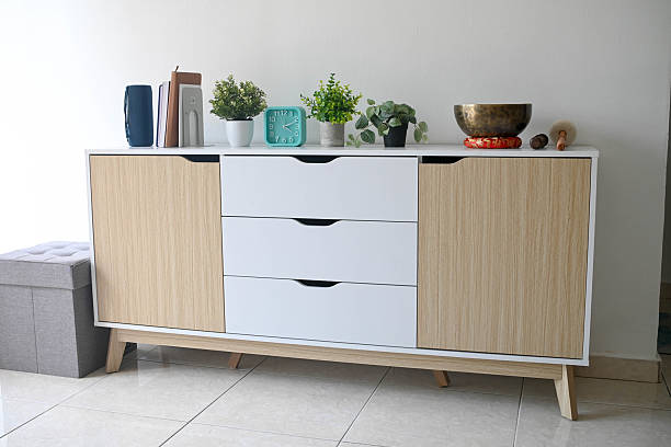 A simple living room showcasing a sideboard cabinet, ceramic tile flooring, and a white wall background.